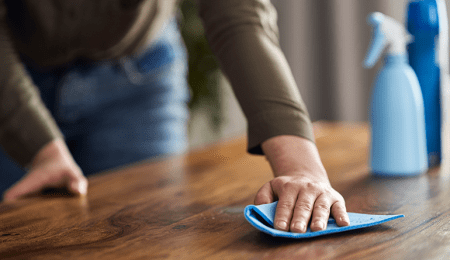 person wiping wood table with cleaning cloth