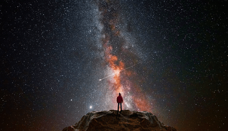 man standing on mound below spectacular view of the galaxy and stars