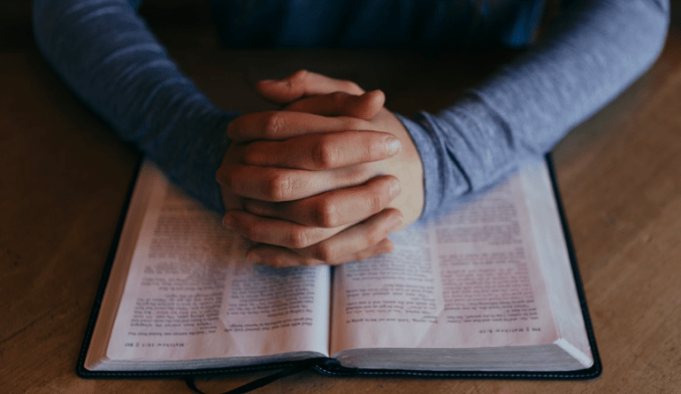 hands clasped over open Bible