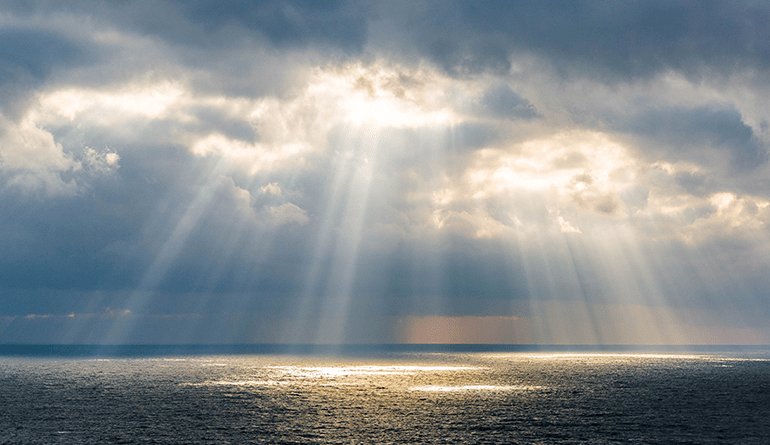 sunbeams shining down out of clouds onto waters of the ocean