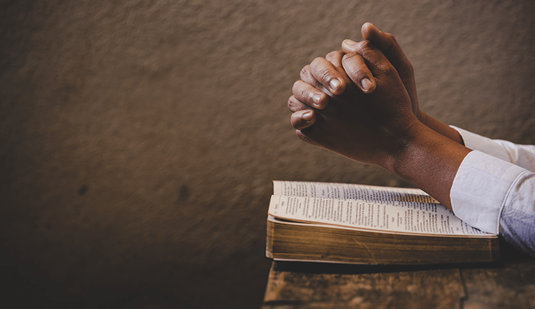 hands clasped over Bible