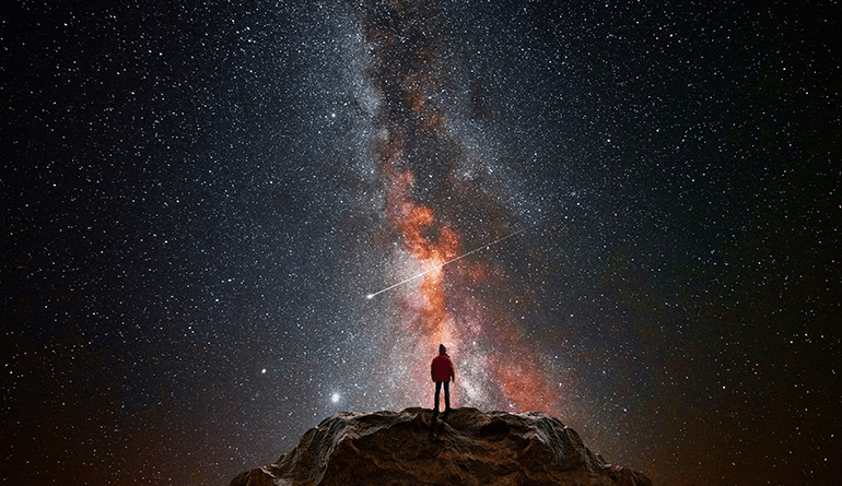 man standing on mound below spectacular view of the galaxy and stars