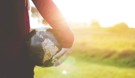 person holding a globe with sunny hillside in background