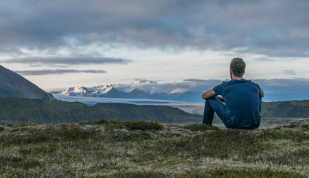 man sitting on ground overlooking mountain view