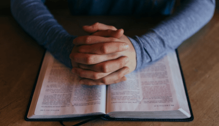 hands clasped over open Bible