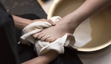 someone drying another's foot with a towel over basin of water