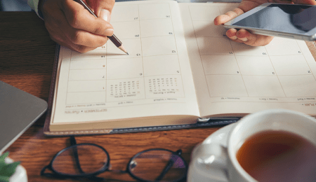 calendar on desk with person pointing to date with a pencil