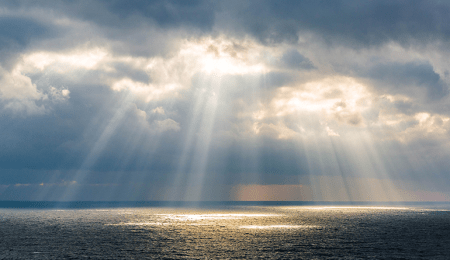 sunbeams shining down out of clouds onto waters of the ocean